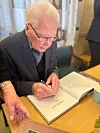 Olav S. Reiersen signerer bøke under lanseringa i Sørhaug bedehus. Foto: Privat