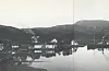 Rutebåten kjem. Det kvite huset på kaien inneheld bustad, landhandel og ekspedisjon. Røyken som stig opp kjem frå bakar Ottesen sitt hus (bnr. 50). Biletet er teke i 1924.