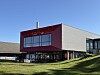 Moderne bygg med store glasvindauge og raud fasade over grønn plen.