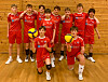 Ungdomslag i raude volleyball-drakter poserer i hall med ballar.