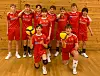 Ungdomslag i raude volleyball-drakter poserer i hall med ballar.