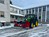 John Deere-traktor med raud snøplog ryddar snø framfor ein bygard