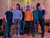 Sju bandmedlemmer står smilande på golvet framfor alterpartiet i ei kyrkje.