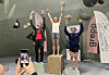 Tre medaljevinnarar på premiepall i klatrehall medan nokon fotograferer dei.