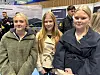 Tre unge kvinner står saman på eit innandørs arrangement.