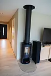 Svart vedomn med stålrøyrpipe i ei moderne stove med TV og høgtalarar.