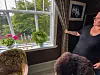 Ei kvinne ved eit stort vindauge med gjenbrukte lister, blomar og eldre møblar.