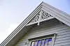 Detalj av eit lyst trehus med handskoren ornamentikk i mønet over eit vindauge.