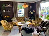 Fargerik stove med forgylte lenestolar, mørk sofa, salongbord, planter og store vindauge.
