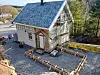 Trebygg under oppføring med grusa uteområde, materialar og eit tilbygg ved inngangspartiet.