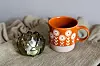 Oransje kopp med blomstermotiv og levande lys på eit mjukt tekstil.