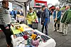 Folk ved ein marknadsstand med honning, tekstilar og andre varer under eit telt.