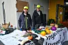 To menn står bak ein stand med grønsaker, matvarer og informasjonsmateriell.