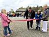 Mann klipper raudt band medan barn og vaksne står rundt på ein grusplass.