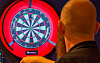 Dartspelar sett bakfrå medan han siktar mot ei raudt opplyst dartskive.