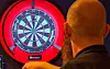 Dartspelar sett bakfrå medan han siktar mot ei raudt opplyst dartskive.