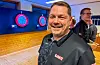 Bjarte Thorkildsen smiler i dartklubben, med dartskiver og ein annan person i bakgrunnen.