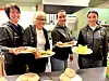 Fire personar viser fram tallerkar med mat i eit kjøkken.