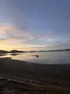 Stille fjord med speglingar, mudderstrand, åsar og fargerik kveldshimmel.
