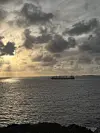 Silhuett av eit lasteskip på havet under dramatiske skyer og låg kveldssol.