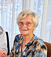 Eldre kvinne med briller og mønstret bluse smiler framfor eit lyst vindauge.