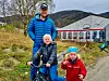 Tre personar framfor eit drivhus i eit grønt fjellandskap.