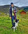 Håkon Rossehaug held hunden Zen i band på ei graseng framfor skogkledde fjell.