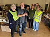 Gruppe frivillige i refleksvestar står mellom bokstabler og esker innandørs.