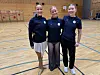 Tre lagveninner poserer på ein handballbane i ein idrettshall.