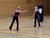 To utøvarar i svarte og rosa klede øver med rekvisittar i ein gymsal.