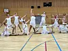 Gruppe utøvarar i kvite klede utfører ein synkronisert oppvisning i ein gymsal.