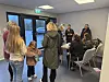 Gruppe menneske i eit lyst lokale med bord, stolar og servering.