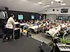 Presentatør ved podium framfor eit stort publikum i eit konferanserom