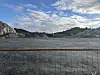 Steinbrot med gjerde i forgrunnen, fjell i bakgrunnen og blå himmel med skyer.