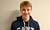 Simen Grinde Flatnes smiler mot kameraet i ein mørk hettegenser.
