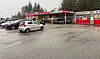 Våt parkeringsplass med fleire bilar framfor eit serviceanlegg merka «BILVASK».