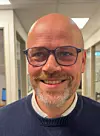 Portrett av Robert Brandvik i Helifuel med briller og mørk genser i ein kontorgang.